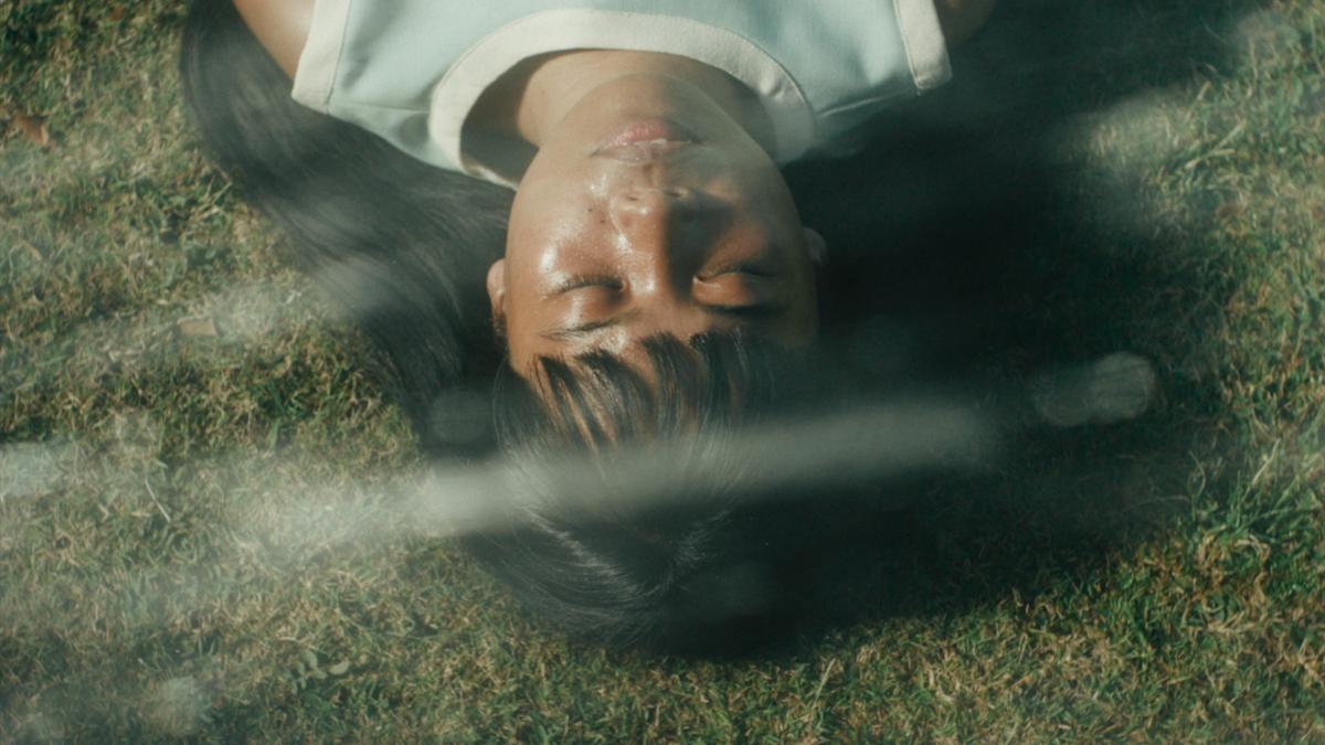 FILIPIÑANA, 2026, young girl with dark hair and bangs lying on grass with eyes shut