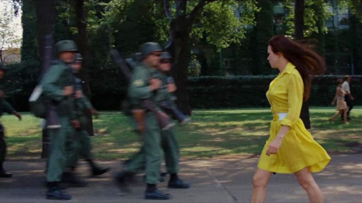 MEDIUM COOL, 1969, woman in yellow dress walking outside in front of armed guards
