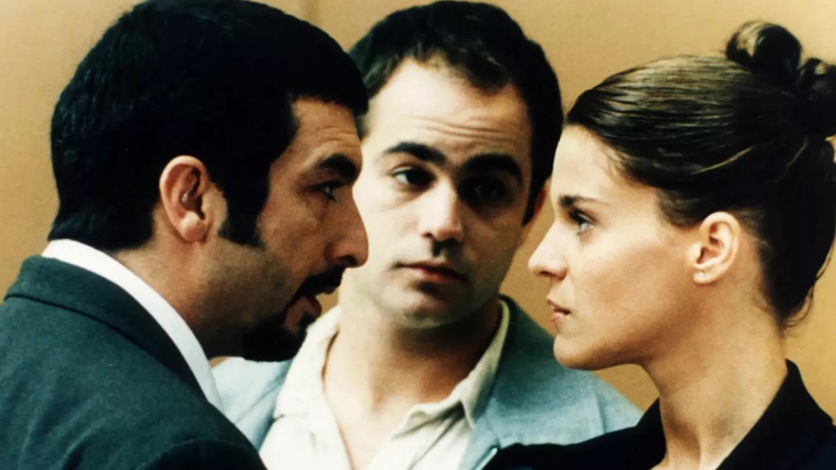 NINE QUEENS, 2000, man and woman in suits looking closely at each other with other man in the background between them