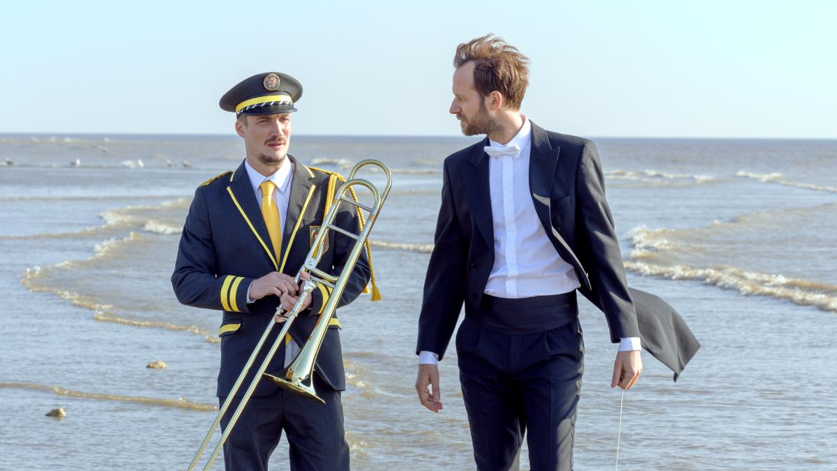 THE MARCHING BAND, 2024, two men in suits on beach holding brass instruments