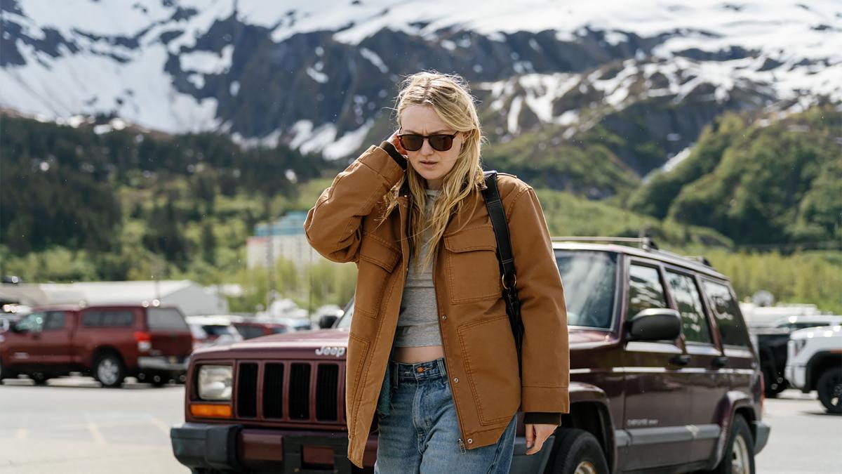 THE SUN NEVER SETS, 2026, Dakota Fanning in brown leather jacket and sunglasses walking in parking lot with mountains in the background