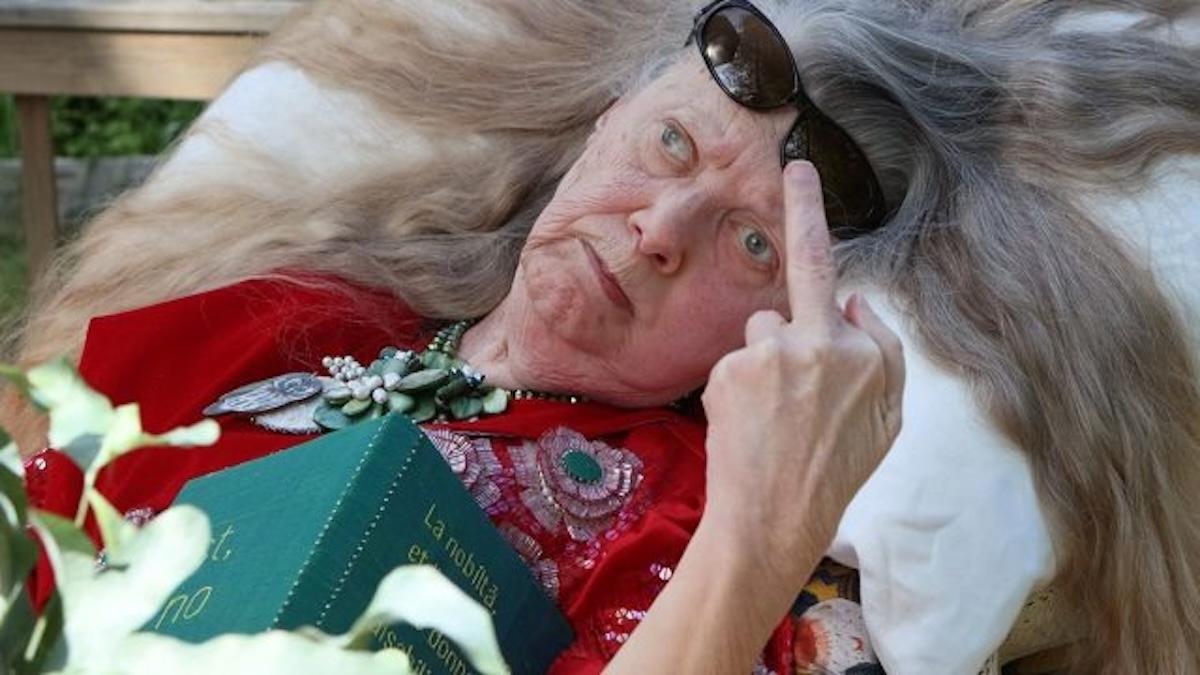 VOICES EMBODIED: PROGNOSTICATION, 2021-26, elderly woman leaning back in chair in red shirt and sunglasses on head with middle finger raised to camera