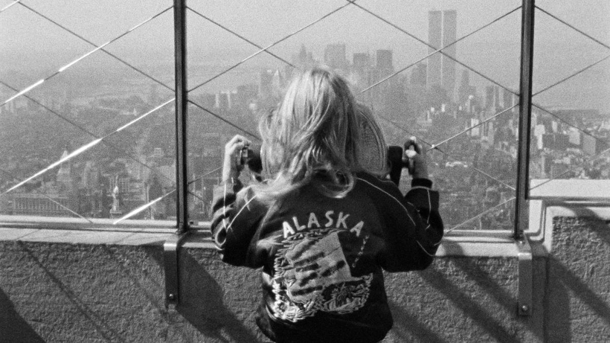 ALICE IN THE CITIES, 1974, black and white image of young girl wearing leather jacket looking over fence from top of tall building