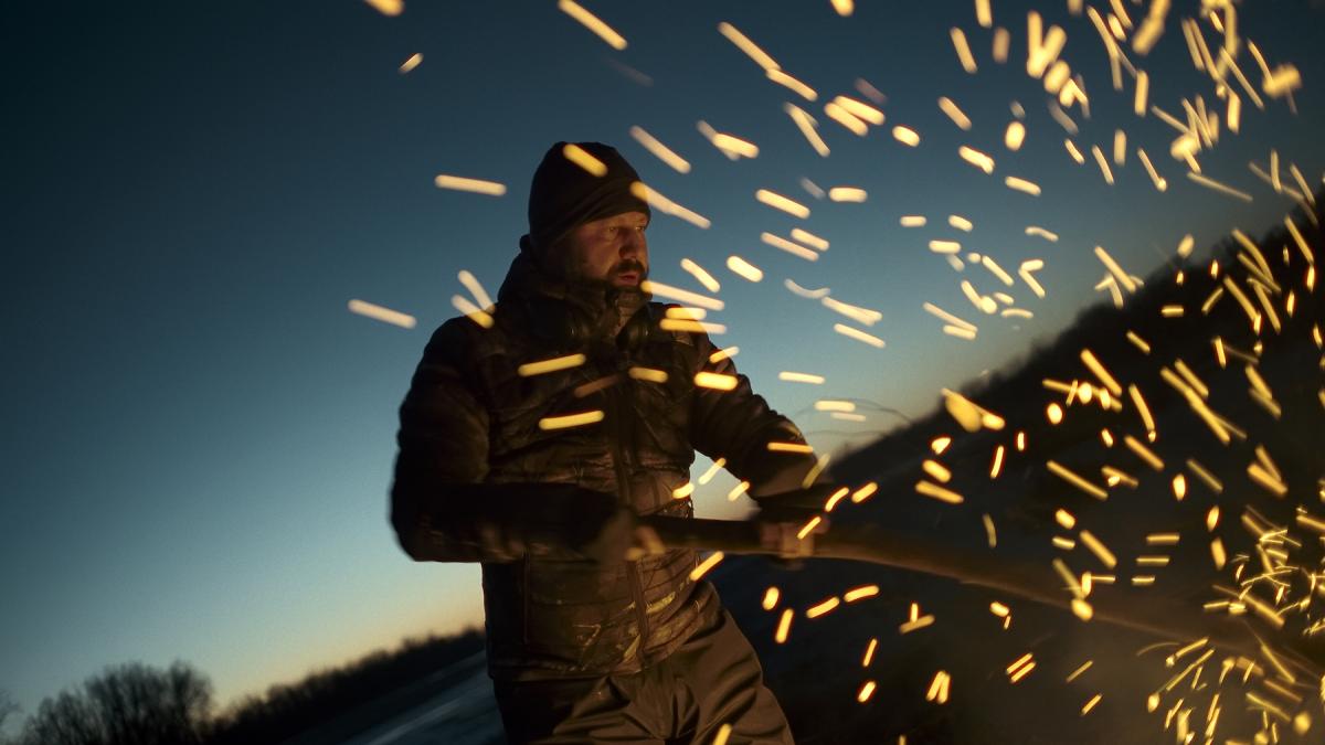 CLOSURE, 2026, man in jacket with sparks flying around him and setting sun at dusk behind him