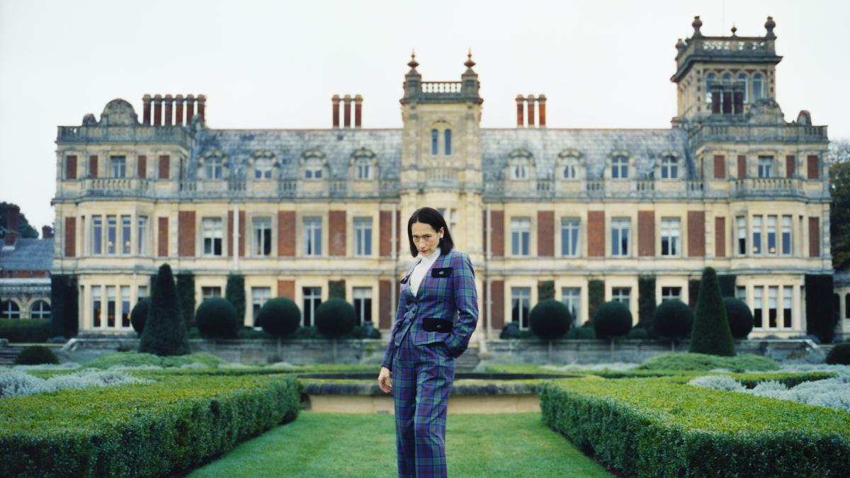 LADY, 2026, woman in suit standing in gardens in front of large palacial building