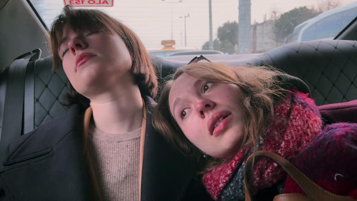 MY UNDESIRABLE FRIENDS: PART II - EXILE, 2026, two young women in back seat of car looking tired with one leaning on other's shoulder