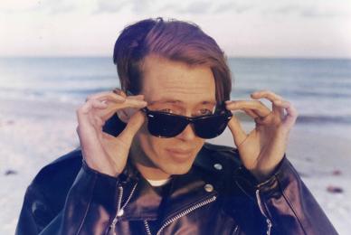 man on the beach in leather jacket and lowering his sunglasses