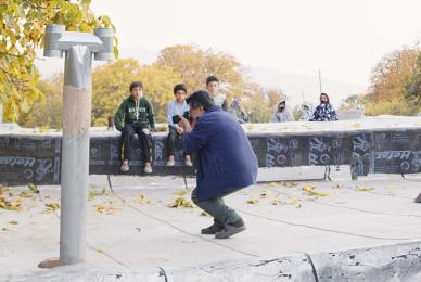 man in public park wearing dress clothes and squatting down aiming camera