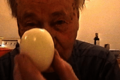 man up close to camera holding round egg in front of face and camera