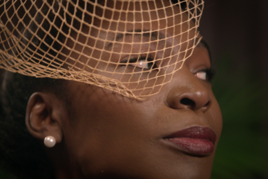 close up of Black woman looking sideways with orange mesh veil in front of face
