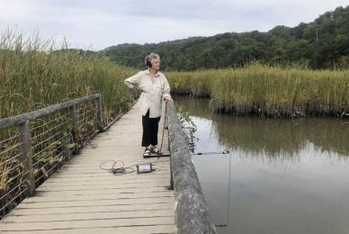 woman standing on bridge near water and marsh wearing headphones
