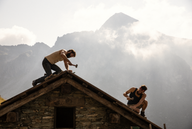 two men working on roof in front of mountains