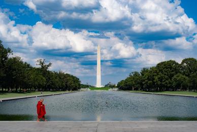 monk in red robe walking across sidewalk in front of washington monument