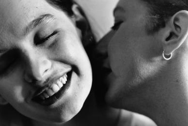 woman smiling and woman next to her whispering closely in her ear