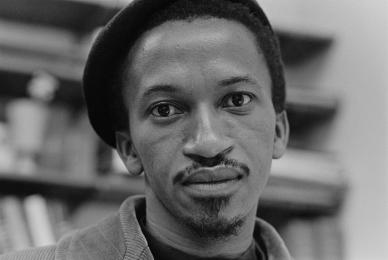 black and white photo of Black man wearing hat in front of bookshelves